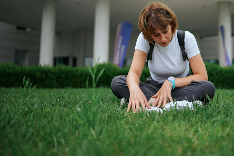 Une jeune femme lit ou ouvrage assise sur l'herbe devant une institution universitaire