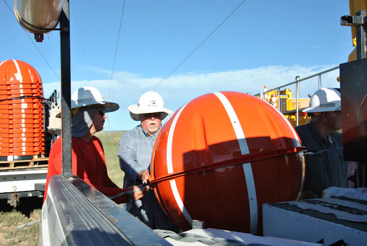 ¿Qué son esas bolas naranjas en algunas líneas eléctricas? 2 Personas con sombreros trabajan con una pelota en la parte trasera de una camioneta.