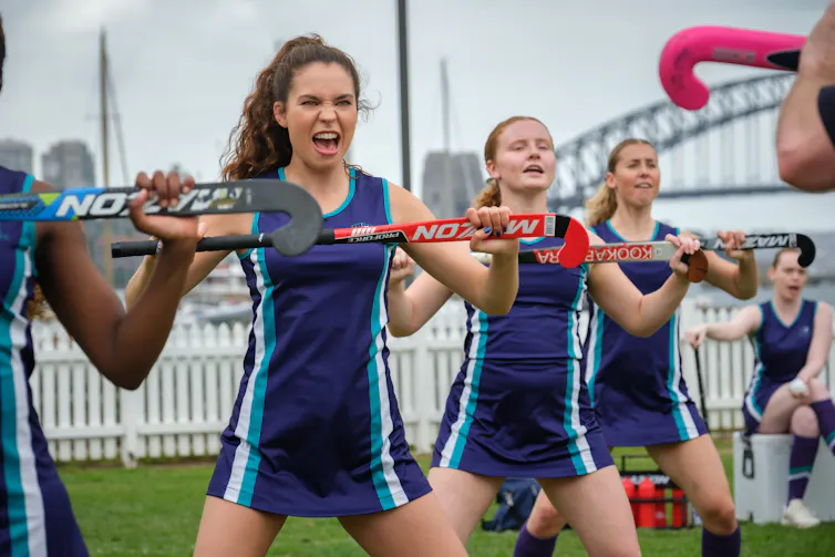Film still: young women in hockey outfits sing.