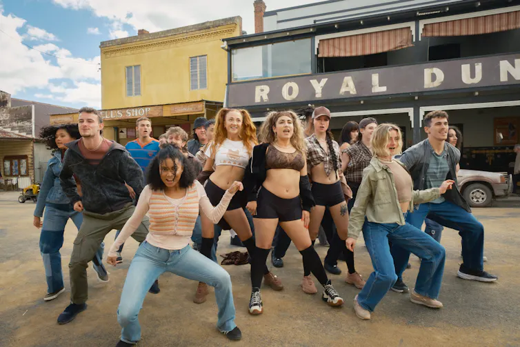 Film still: young people, mostly women, dance on a country town road.