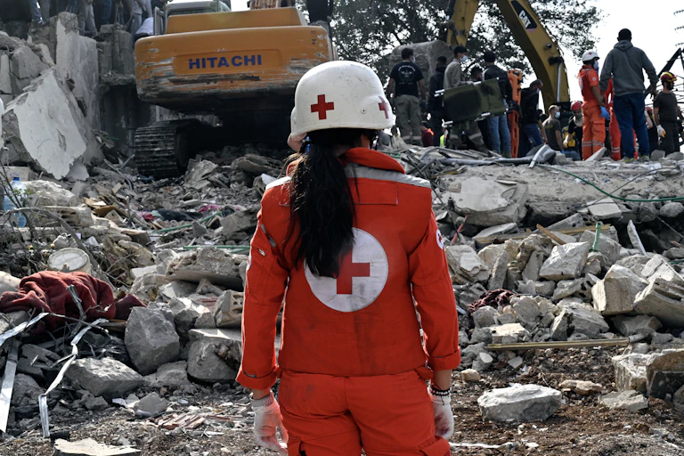 A Red Cross worker looks onto a pile of rubble after a recent military attack.