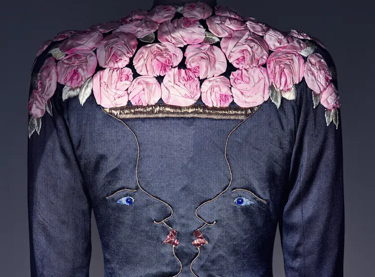 A blue evening coat embroidered with two faces kissing and the shoulders covered in satin pink roses.