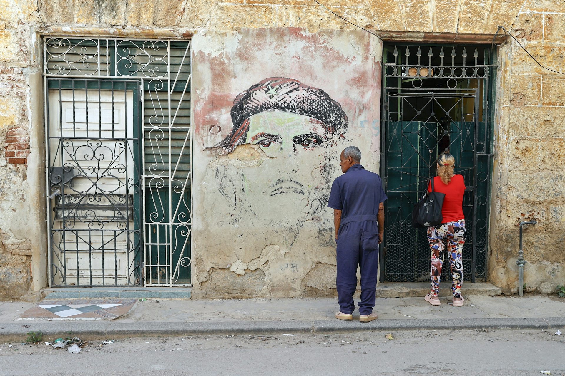 Cubans stand next to a mural depicting Che Guevara in Havana.