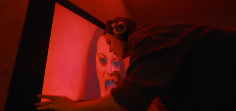 A young woman in headphones against a projection of a scary face on a red background.
