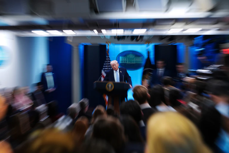 A zoom lens captures a man at a lectern during a press conference.