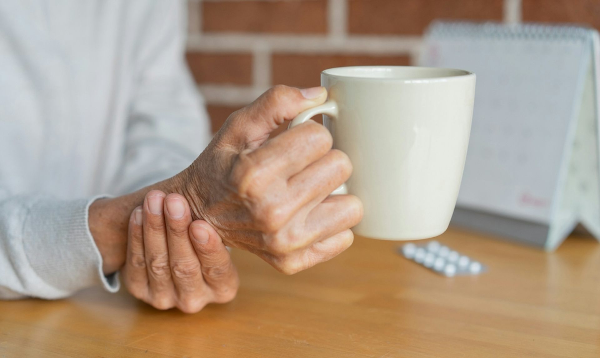 A person holding a mug, their other hand supporting their wrist.