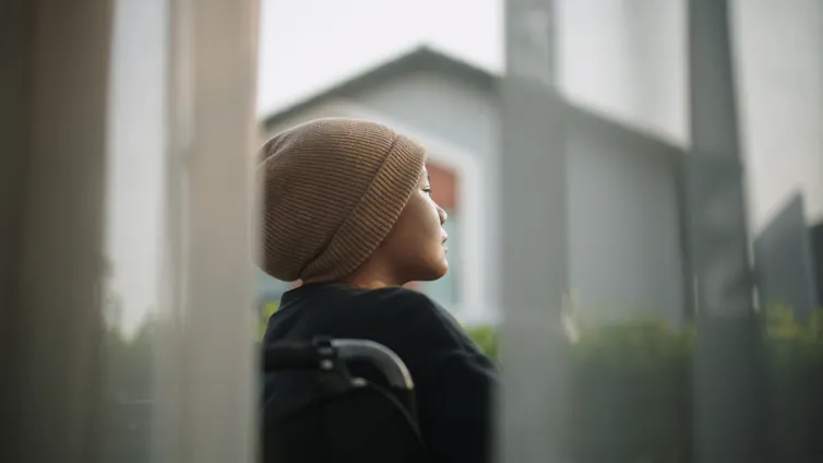 woman wearing hat seated in wheelchair looks outside