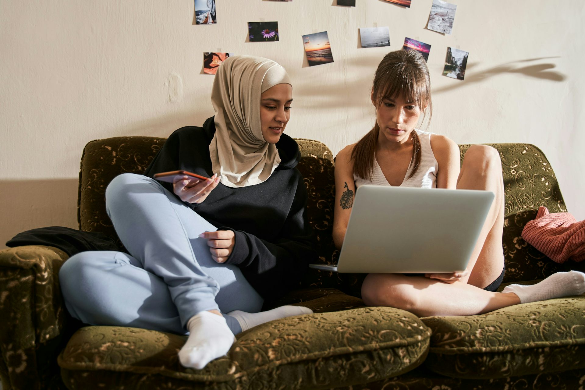 Two young women sitting on a couch looking at a laptop screen together.
