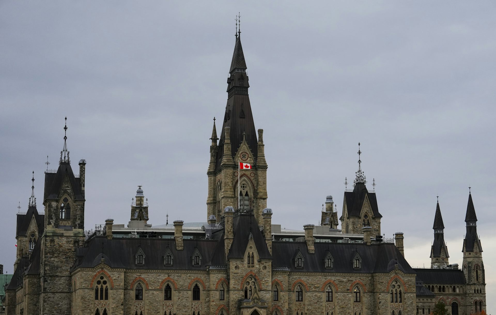 A maple leaft flag flying over a roof with tower peaks. 