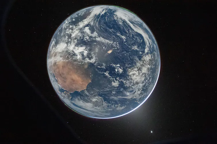 Uma imagem da Terra vista do espaço, com um ponto no canto inferior direito indicando um reflexo da janela da espaçonave.
