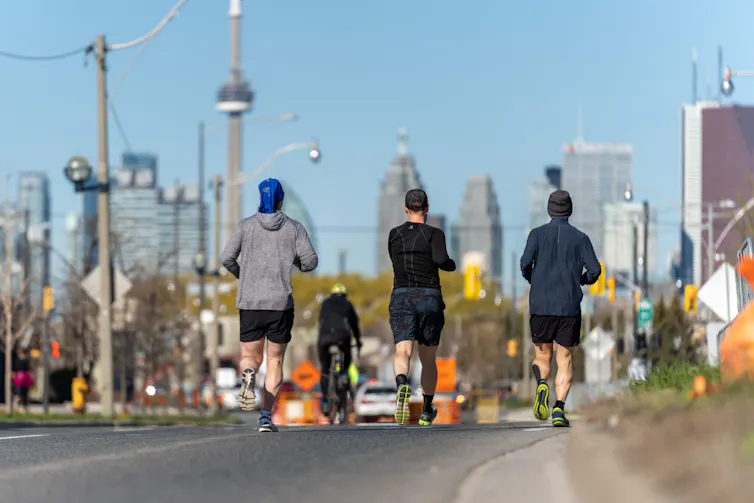 Tres personas corriendo juntas en una pista, la Torre CN y edificios altos al fondo