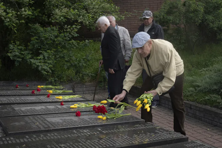 Cuarenta años después del desastre de Chernóbil, su legado aún resuena 1 hombres mayores depositan flores en las tumbas