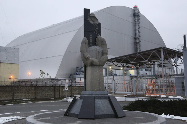 A statue of open hands holding a cube in front of a large metallic dome structure