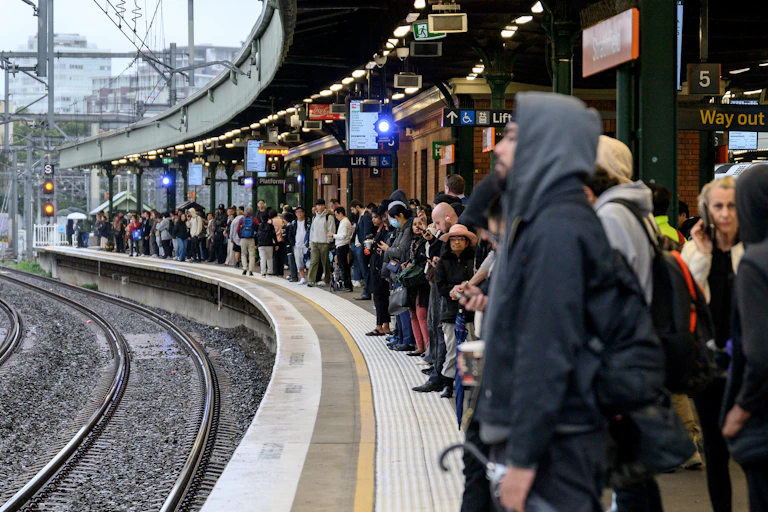 Commuters wait on a train station platform.