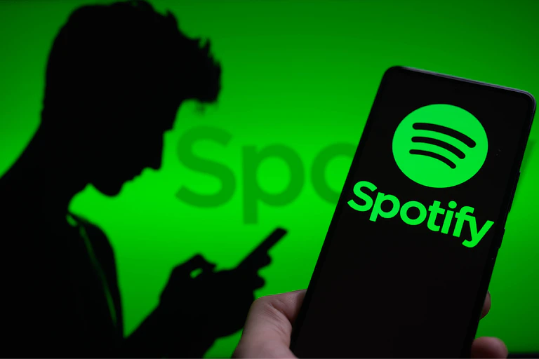 The Spotify logo is displayed on a smartphone with the word 'Spotify' visible in the green background.There is a silhouette of a man to the left.