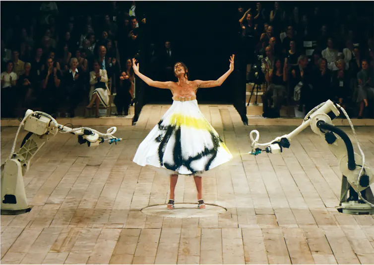 A model in a white dress being sprayed by robots.