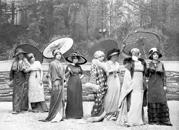 A black and white image of a group of early 20th century fashion models lined up in a garden.