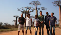 Six smiling people standing on a road in front of baobabs