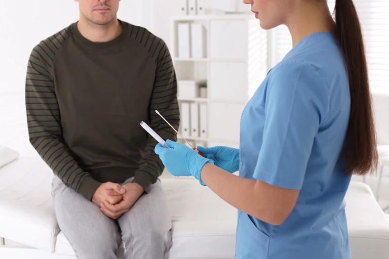 Un hombre en una consulta y, en primer plano, una enfermera o doctora con una prueba en sus manos