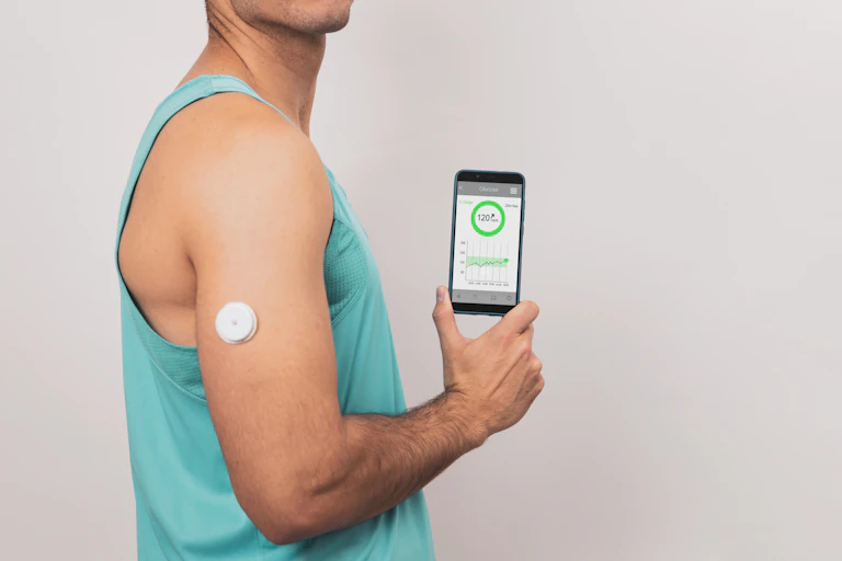 A man in a gym shirt wears a sensor for a continuous glucose monitor on his upper arm and shows his mobile phone displaying his glucose numbers.