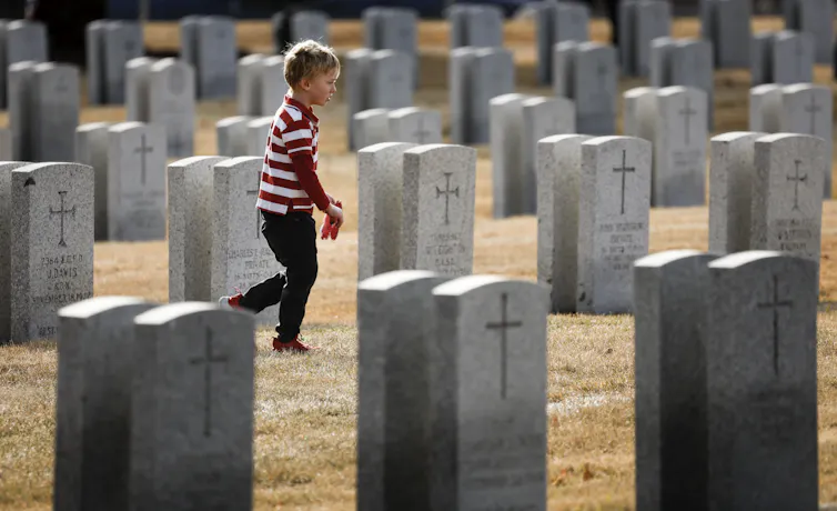 Un niño con una camisa a rayas rojas y blancas lleva una amapola de papel a través de las lápidas de los soldados.