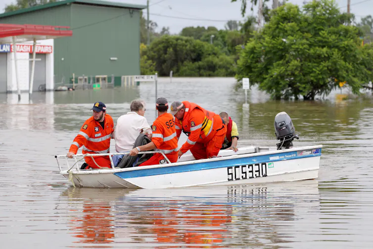 People in orange uniforms in a boat in a flooded town.