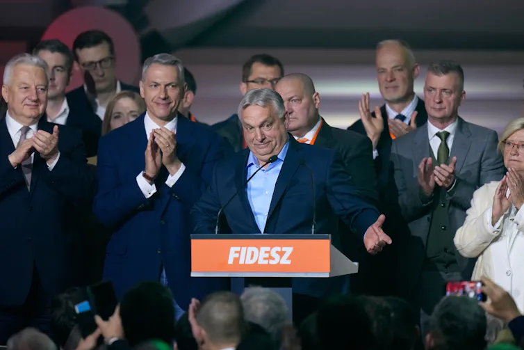 a man with grey hair in a middle part surrounded by othe men applauding