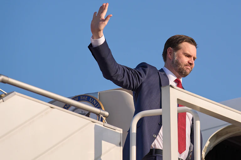 A man in a suit waves as he boards an airplane