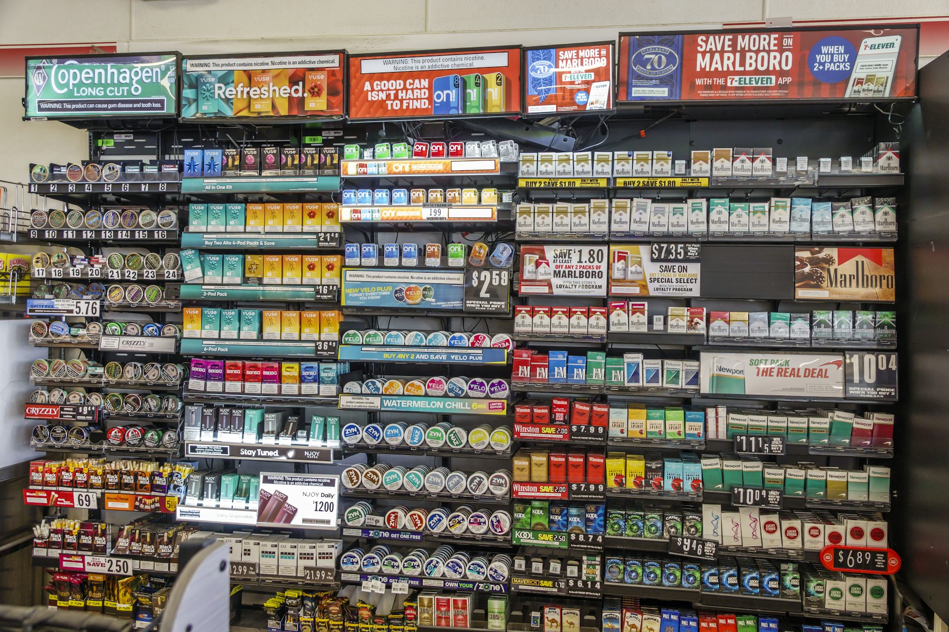 Uma parede repleta de prateleiras exibe uma variedade de marcas de cigarros, além de outros produtos que contêm nicotina.