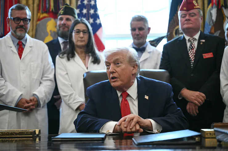 A man sitting at a desk is surrounded by people wearing white medical coats.