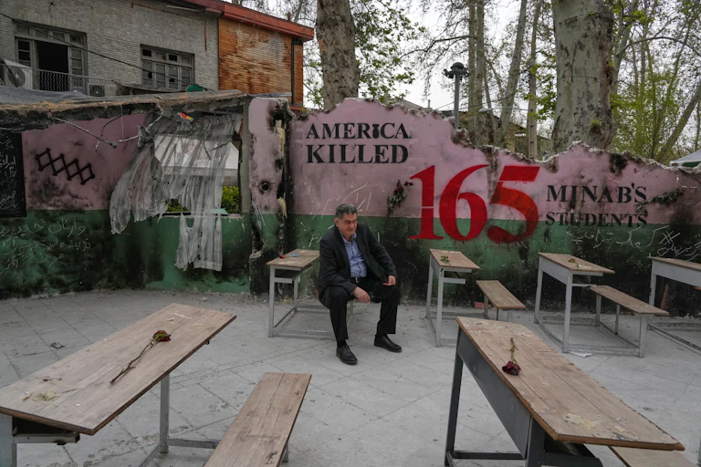 A man sits on a bench. Behind him a mural reads 'America killed 165.'