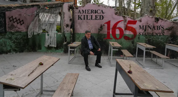 A man sits on a bench. Behind him a mural reads 'America killed 165.'