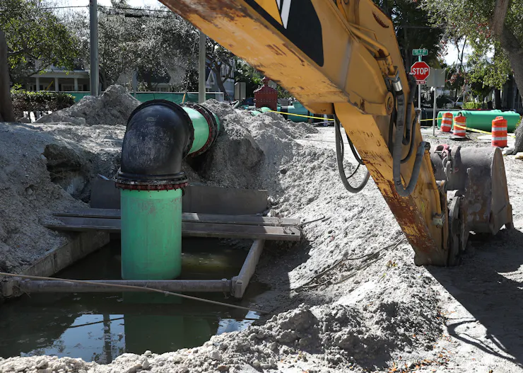 A large pipe emerges from the ground and then goes back in, with a piece of construction equipment in the foreground.