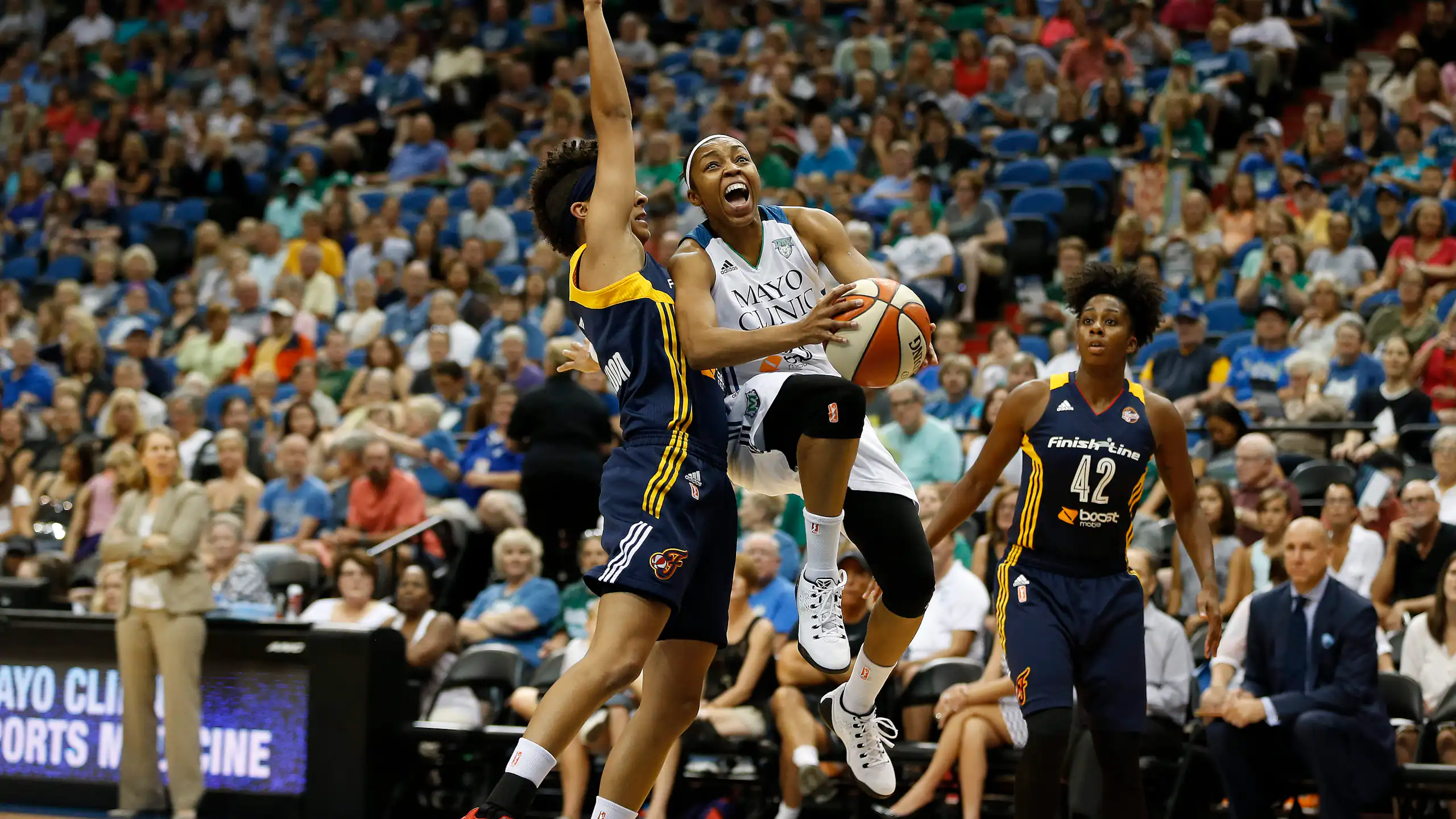 Two WNBA Indiana Fever guards, Layshia Clarendon and Shenise Johnson, try to stop Minnesota Lynx guard Renee Montgomery from scoring at a WNBA basketball game.