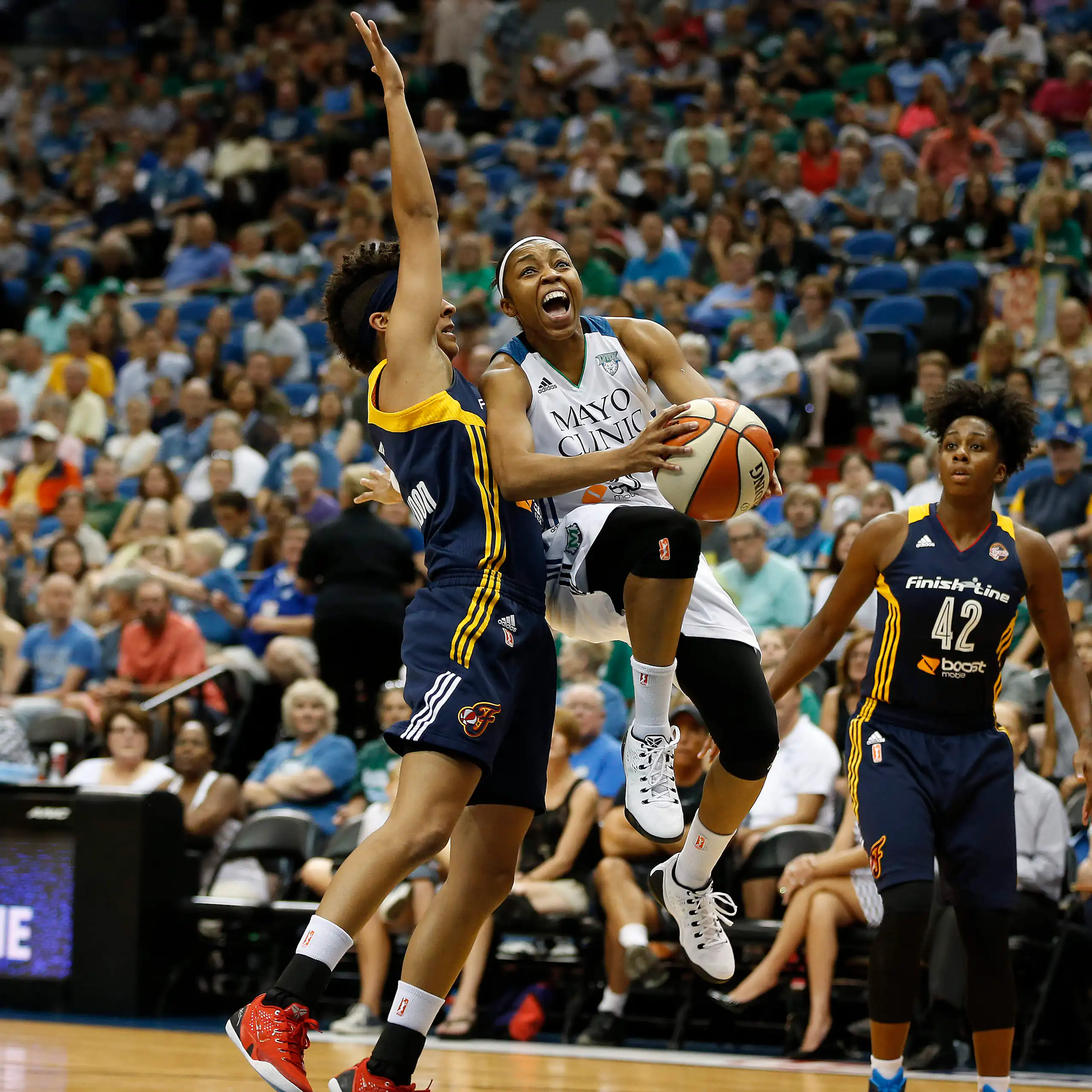 Two WNBA Indiana Fever guards, Layshia Clarendon and Shenise Johnson, try to stop Minnesota Lynx guard Renee Montgomery from scoring at a WNBA basketball game.