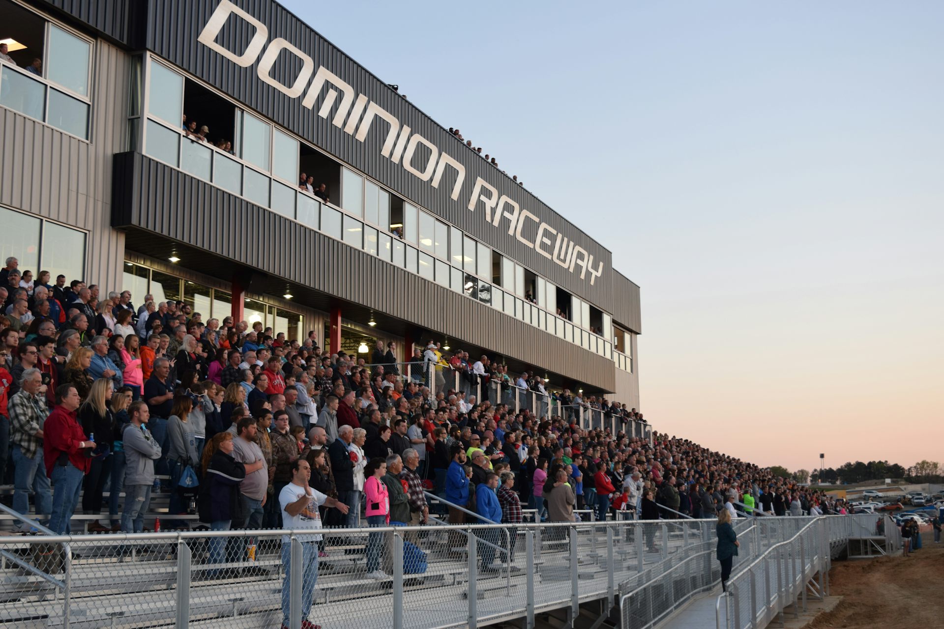 Fans in the stands cheer during a motorsport event at dusk.