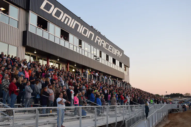 Fans in the stands cheer during a motorsport event at dusk.