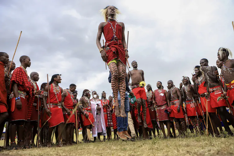 two men in red robes jumping, others stand in a circle around them