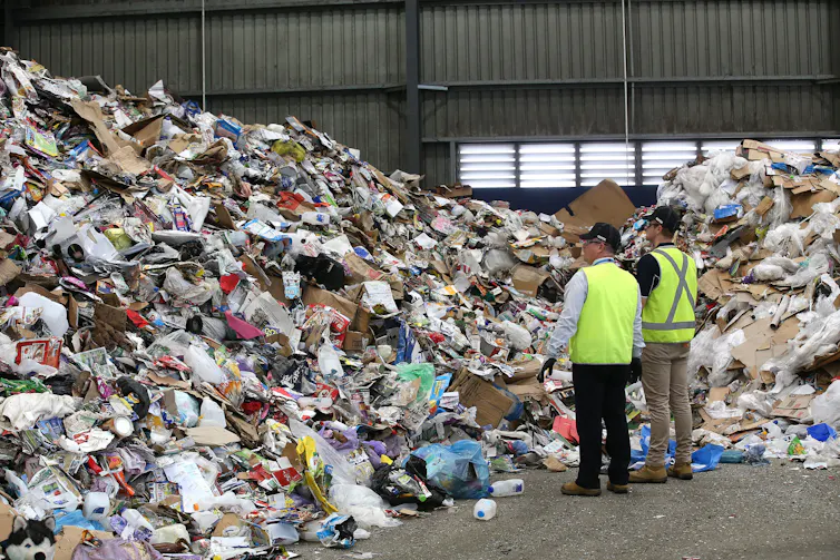Two men stare at a giant pile of rubbish destined for landfill.