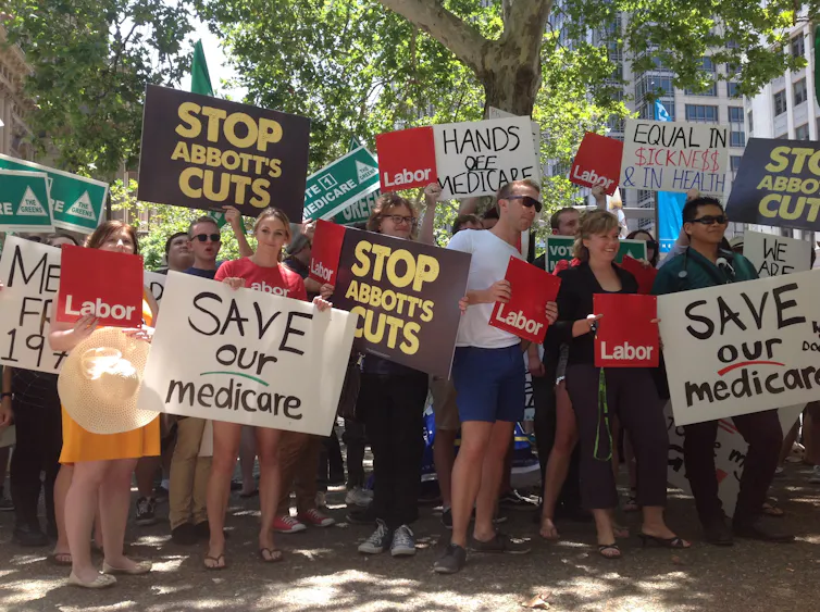 A crowd of protesters hold up signs saying save our medicare
