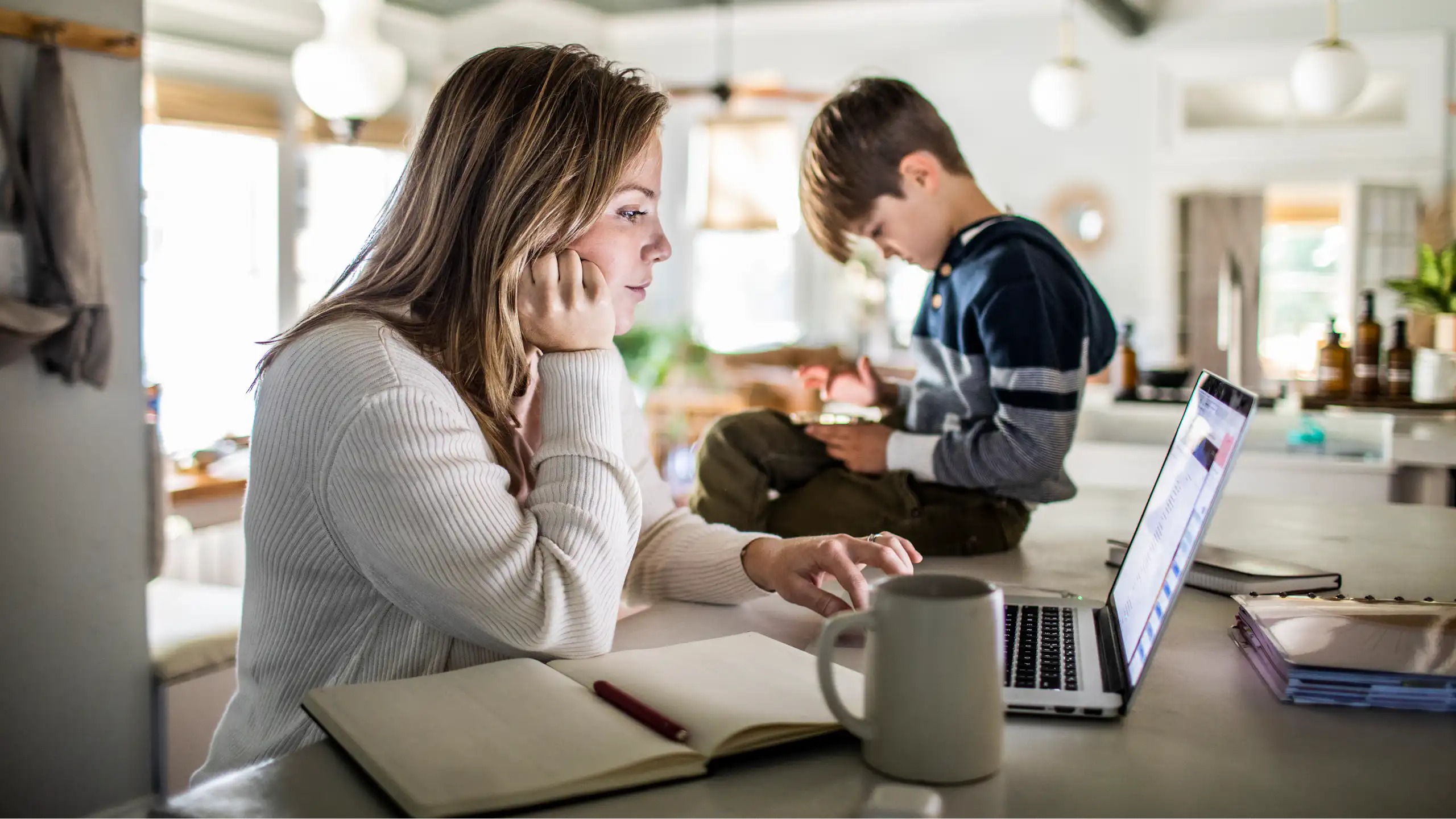 Woman works on laptop with her son sitting on the table next to her