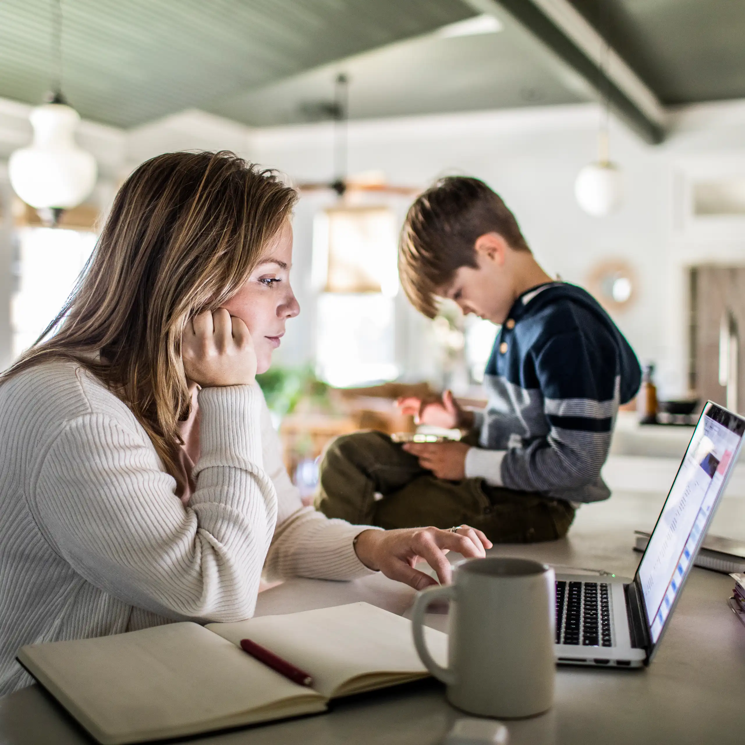 Woman works on laptop with her son sitting on the table next to her