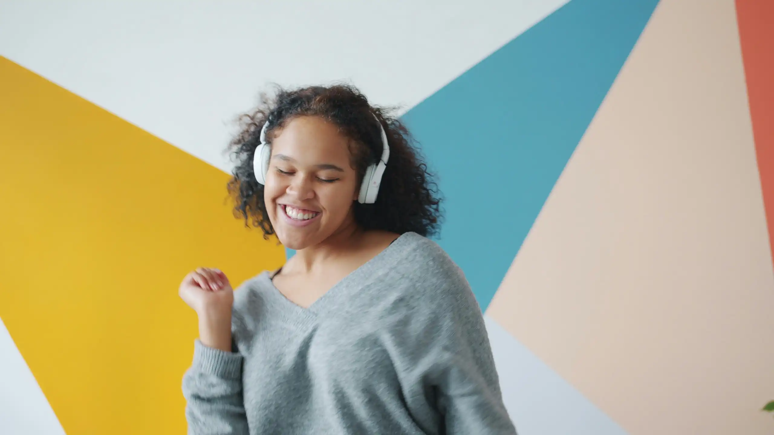 Une jeune femme danse en écoutant de la musique, avec un mur coloré en arrière-plan.