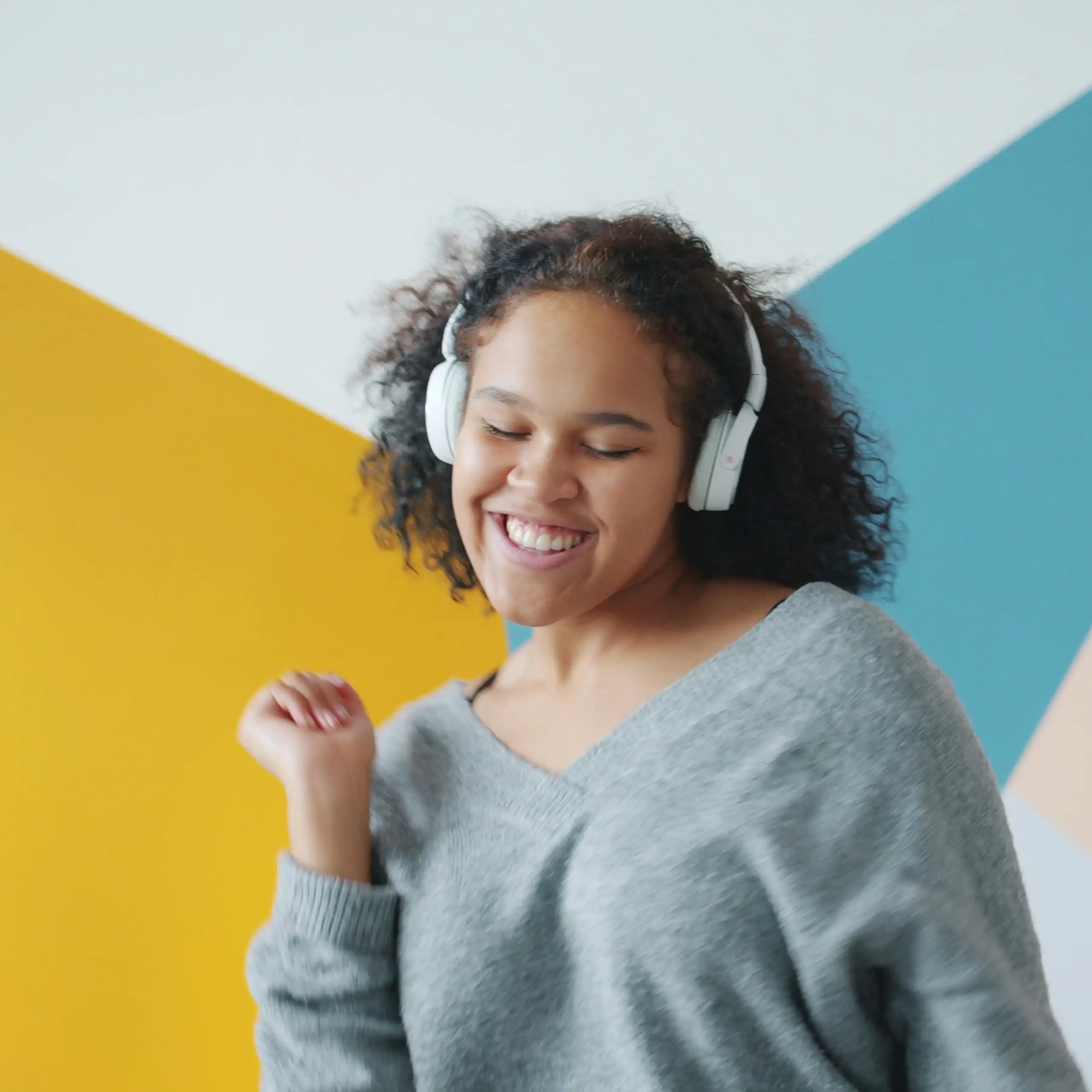 Une jeune femme danse en écoutant de la musique, avec un mur coloré en arrière-plan.
