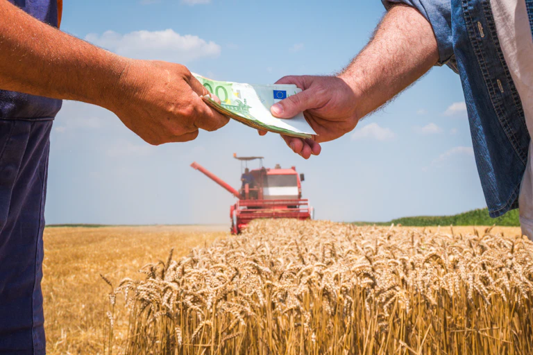 Deux hommes se donnant des billets d'euros devant un champ agricole.