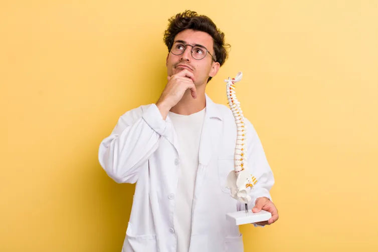A puzzled doctor holds a spine and hip bones.