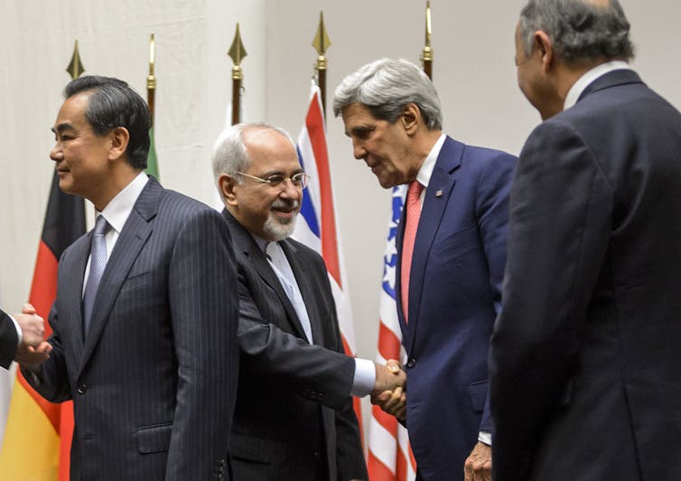 Four men oin suits shake hands.