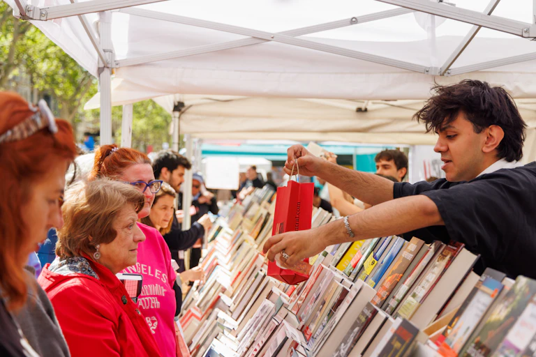 Un dependiente de una caseta de libros le da una bolsa de papel a una mujer.