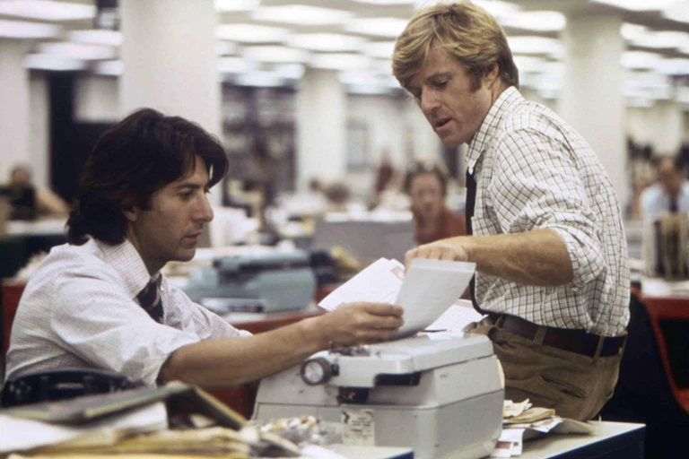 Two men sitting a desk reading papers in a newspaper office.
