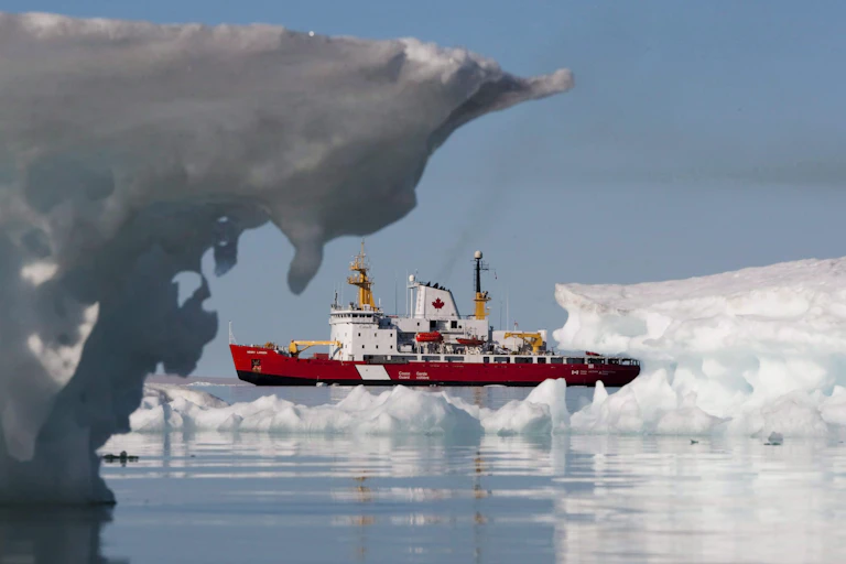 A red and white ship with a red maple leaf passes icebergs